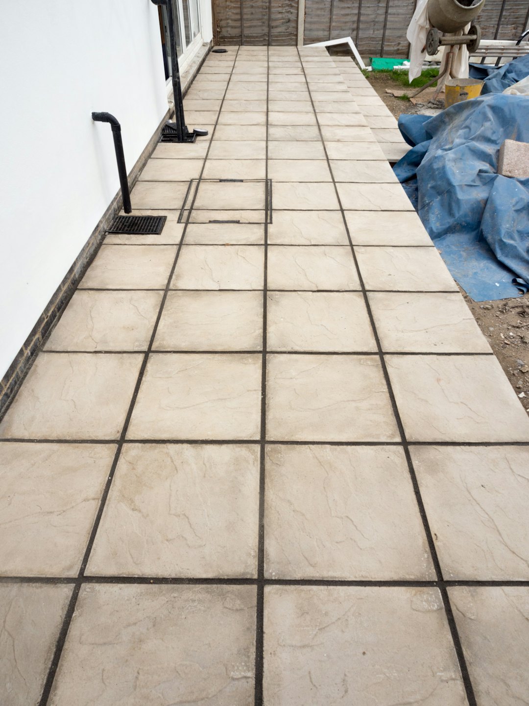 Newly laid beige patio slabs sit beside a white house wall.