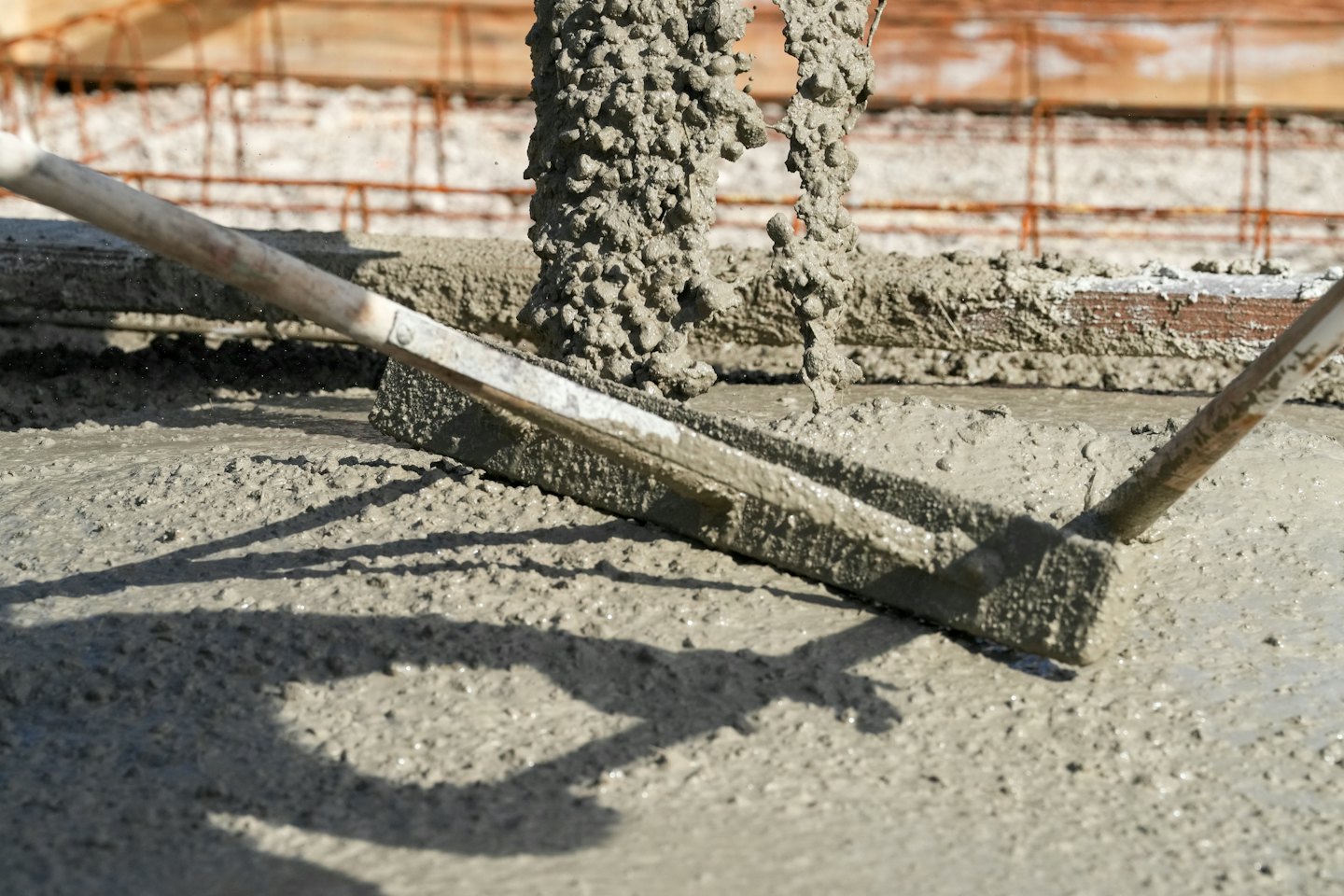 Worker screeding wet concrete on a sunny construction site.