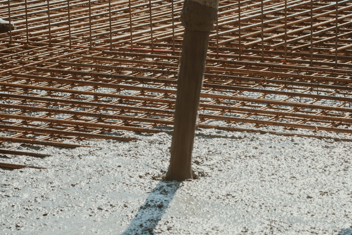 Wet concrete pours from a chute onto rusted rebar grids.